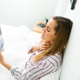 Woman talking virtually to doctor holding throat