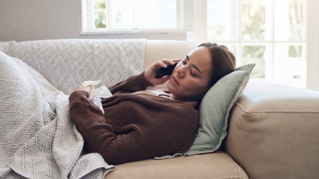 Shot of a young woman talking on a cellphone while feeling sick at home