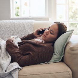 Shot of a young woman talking on a cellphone while feeling sick at home