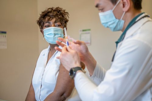 Un medic se pregătește să injecteze brațul unei femei în vârstă cu o doză de vaccin.