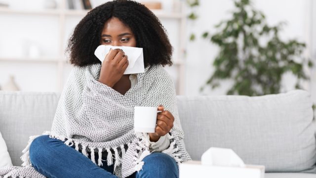 Woman wrapped in blanket blowing her running nose
