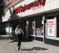 A woman wearing a face mask walks in front of a CVS pharmacy Midtown with a sigh advertising free flu shots.