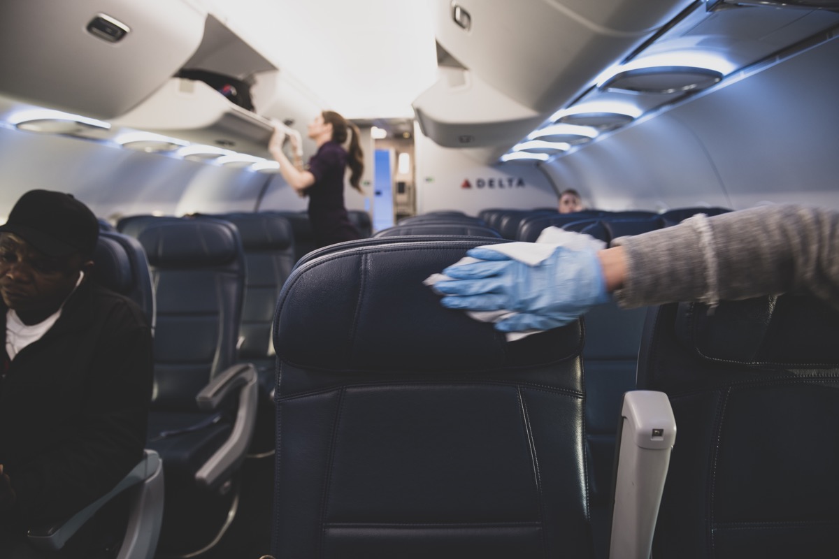 On a Delta flight from New York's Laguardia Airport to Atlanta, a passenger who has just boarded wears a plastic glove while using a wipe to disinfect the airplane seats and armrests on her row.  (March 21, 2020)