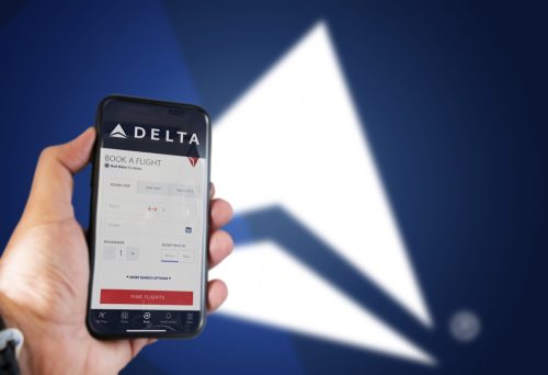 Hand holding a phone with Delta Airlines flight booking application. Delta logo blurred on a blue background. Delta Airlines is one of the major airlines in the US
