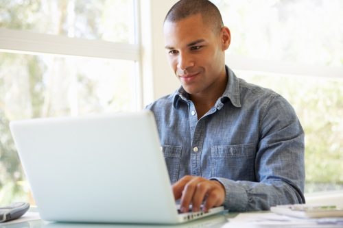 Young man using laptop at home looking at screen