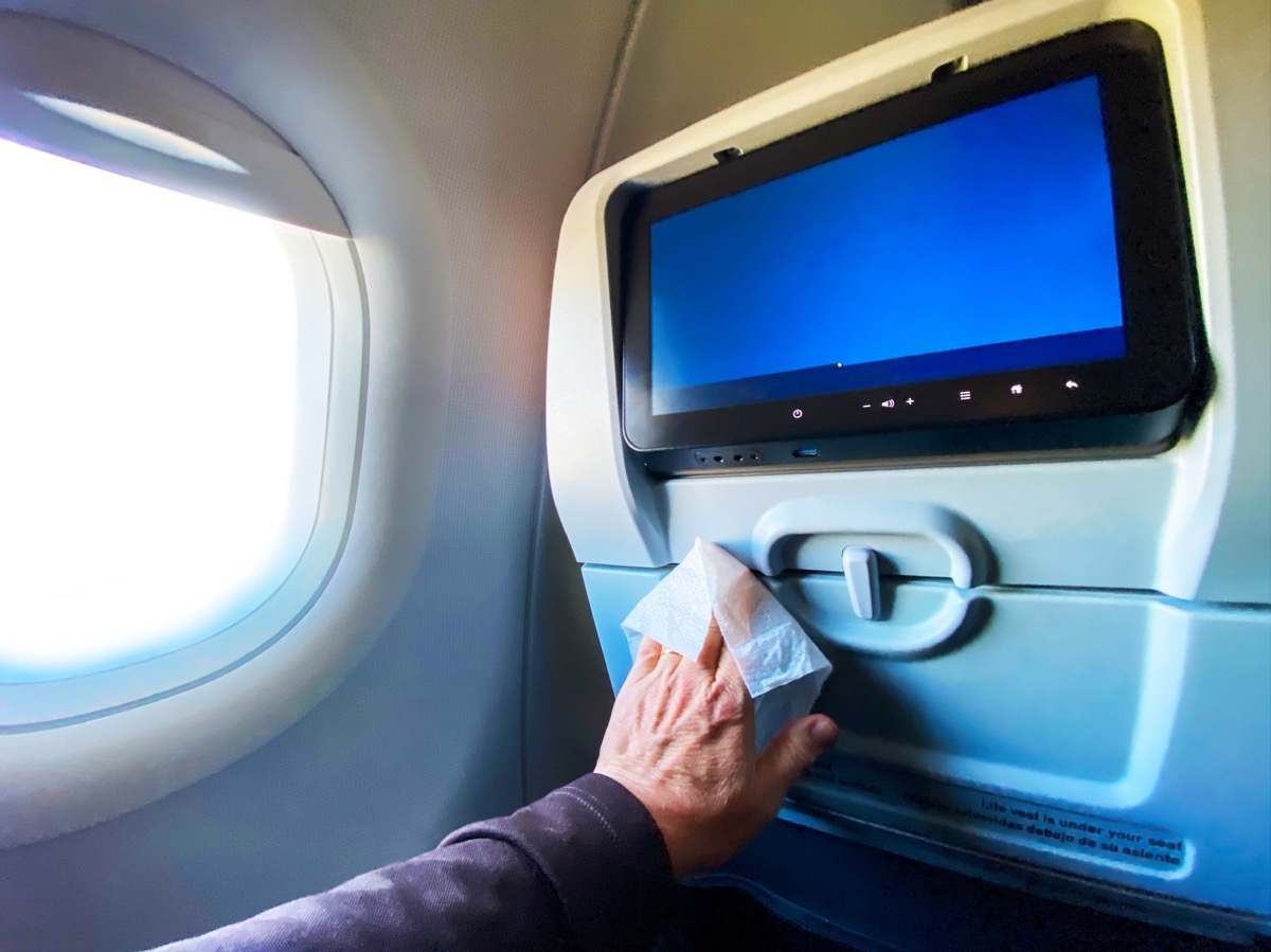 close-up of hand with disinfectant wipe on tray table in airplane