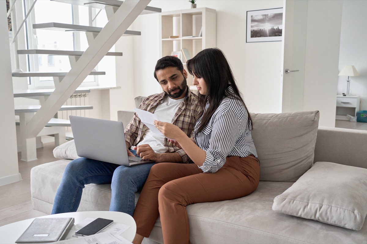 couple sitting on couch checking paper bills and using laptop