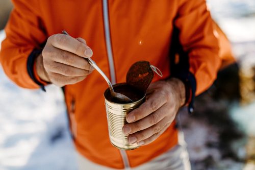 Tourist hiker eating canned food on winter hiking on snowy winter day