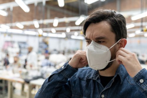 homem trabalhando em fábrica têxtil durante a pandemia COVID-19 e consertando sua máscara facial