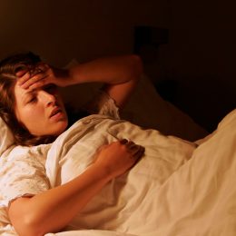 A woman in the bed expressing headache. Nighttime.
