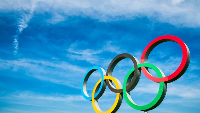 A statue of the Olympic rings set against a blue sky