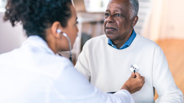 A doctor listening to the heartbeat of a senior man by using a stethoscope
