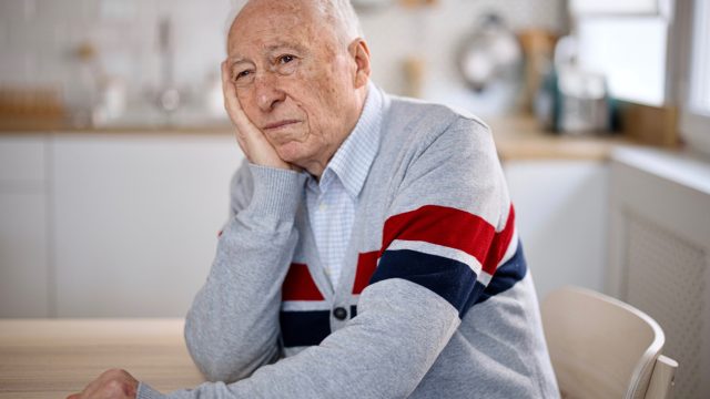 A senior man sitting in his kitchen with a look of apathy