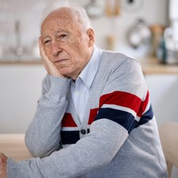 A senior man sitting in his kitchen with a look of apathy