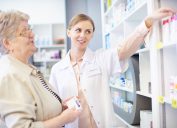 A senior woman picking up prescriptions in a pharmacy while speaking with a pharmacist
