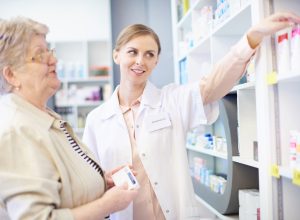 A senior woman picking up prescriptions in a pharmacy while speaking with a pharmacist