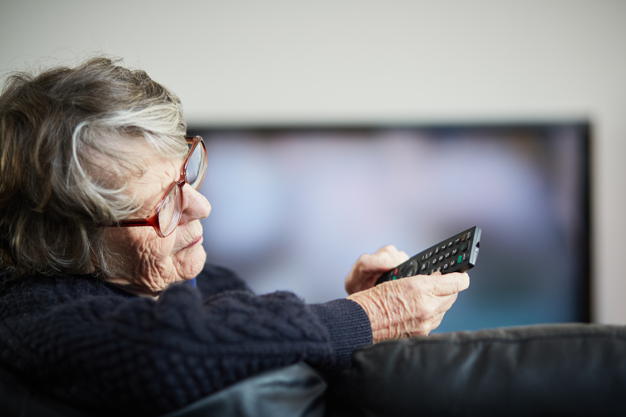 A senior woman looking at her remote control while watching TV