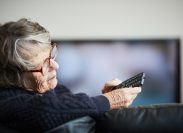 A senior woman looking at her remote control while watching TV
