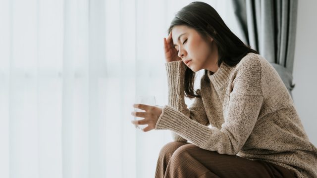 woman feeling headache from flu and cold holding a glass of water, health problems treatment