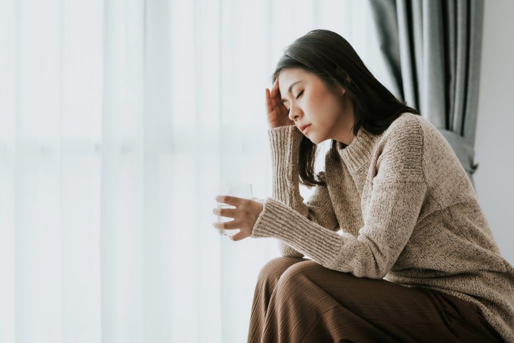 woman feeling headache from flu and cold holding a glass of water, health problems treatment