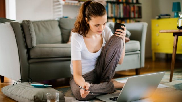 Fotografie cu o tânără care stă pe podea și lucrează la laptop