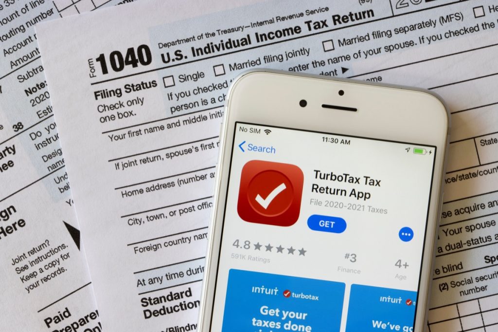 the TurboTax Tax Return App icon is seen on an iPhone atop the form 1040, U.S. Individual Income Tax Return.
