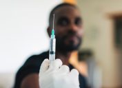 Close-up of a doctor vaccinating young man at home for covid-19 immunization. Female doctor hand holding syringe for preparing Covid-19 vaccine.