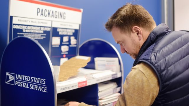 Mature man at the post office chooses an packaging - envelope or box for mailing. Postal system of the United States