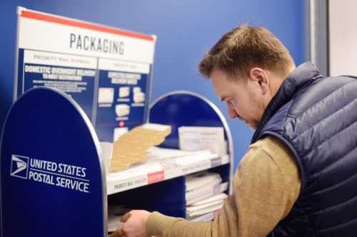 Ein reifer Mann bei der Post wählt ein Paket aus - einen Umschlag oder einen Briefkasten.  Postsystem der Vereinigten Staaten