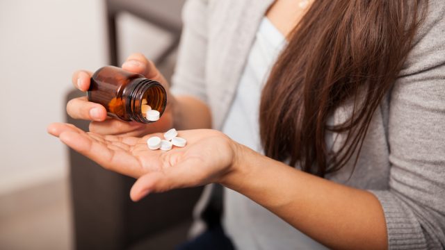 A woman pouring aspirin tablets into her hand out of a pill bottle