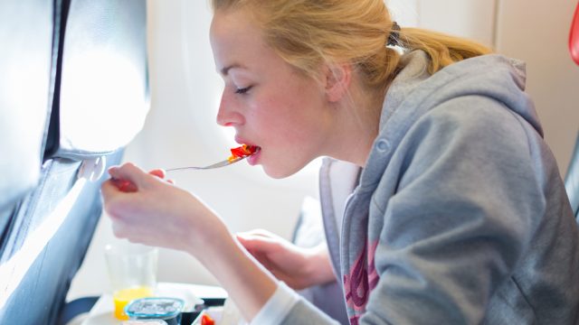 A young woman eating a meal on a commercial airplane flight