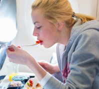 A young woman eating a meal on a commercial airplane flight