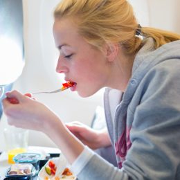 A young woman eating a meal on a commercial airplane flight