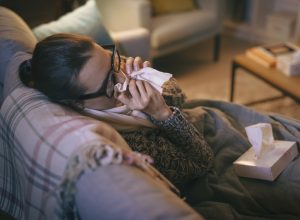 A young woman blowing her nose while sick on the couch with COVID or the flu