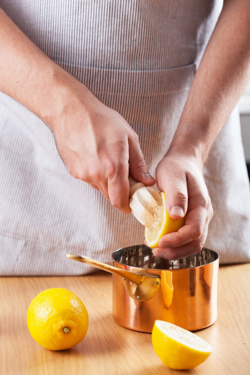 man squeezing lemon into a copper pot