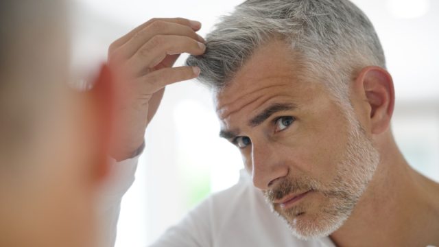 40-year-old man checking hair in front of mirror