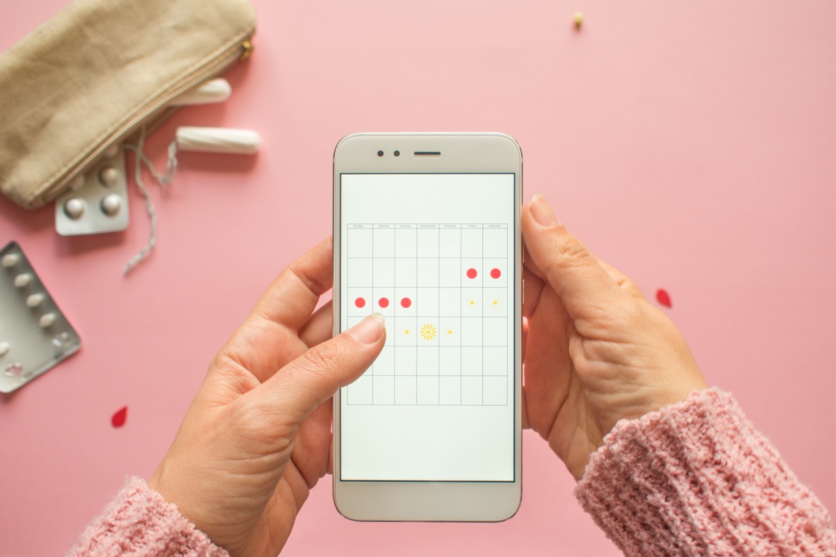 Woman tracking her period on phone, pink background