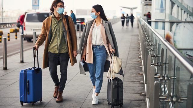 A couple entering the airport with their luggage while wearing masks