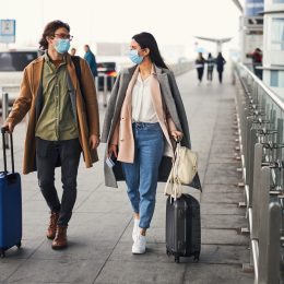 A couple entering the airport with their luggage while wearing masks