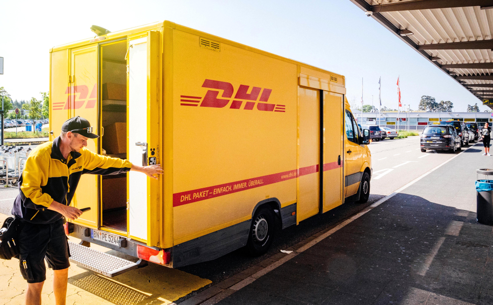 A delivery driver standing behind a DHL delivery truck