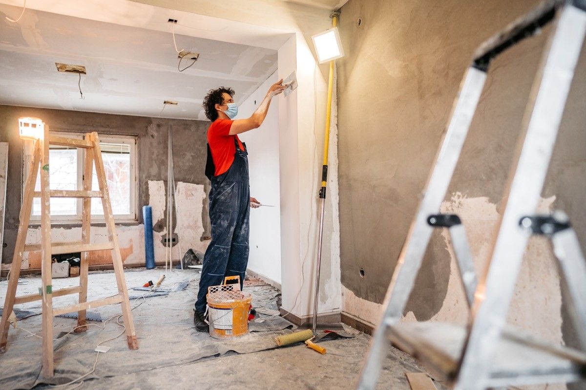 Construction worker plastering and smoothing concrete wall in room. Renovating apartment.