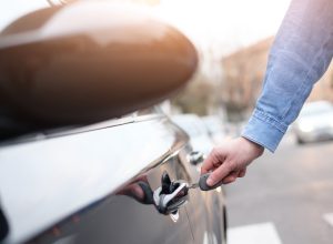 A person locking or opening a car door on the street with a key