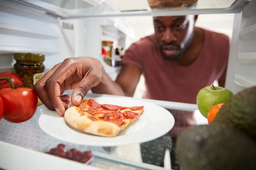 A man reaching into the fridge for a slice of leftover pizza