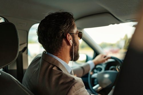 Handsome stylish bearded adult businessman in full suit using headset while driving car