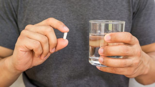 A man holding up a supplement pill next to a glass of water