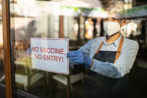 A female restaurant owner holding a sign in the window showing "No vaccine, no entry", meaning that only vaccinated people against COVID-19 can go in.