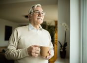 A senior man drinking a cup of coffee or tea from a mug while looking out the window