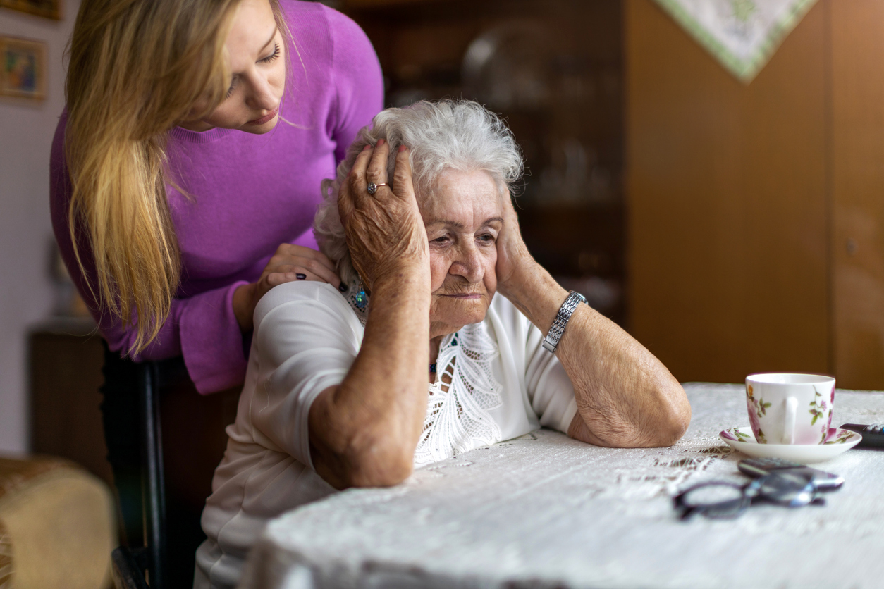 A senior woman sitting while being consoled by her care taker