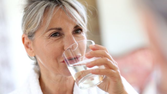 A senior woman drinking a glass of tap water