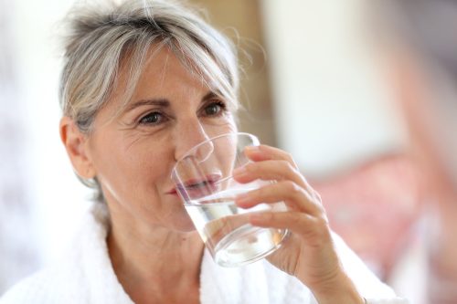 Một phụ nữ cao tuổi uống một cốc nước máy